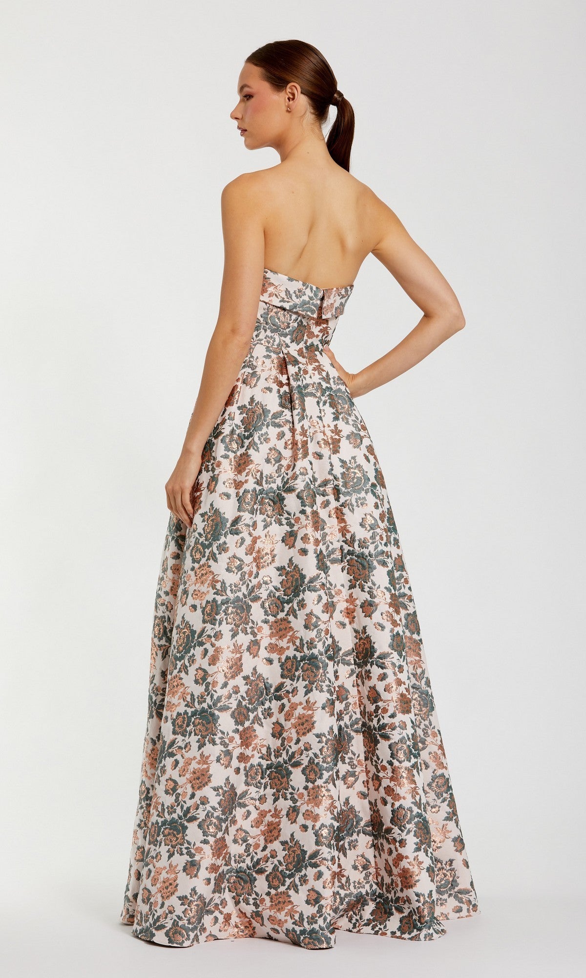 A woman wearing the Long Formal Dress: Mac Duggal 68945, a strapless floral ball gown, stands with one hand on her hip, facing away from the camera.